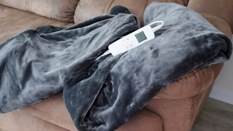 Dark grey electric blanket and controller on brown couch