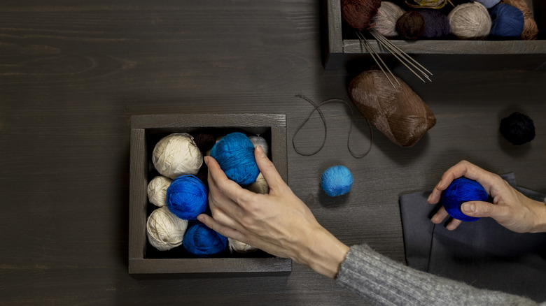 Person placing blue yarn ball onto wall shelf.