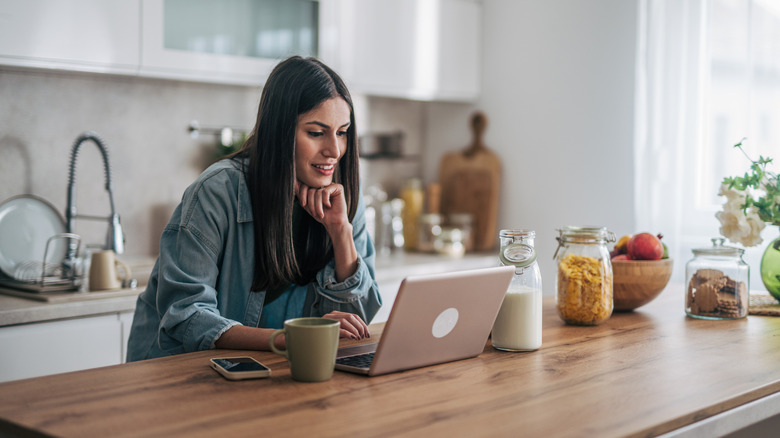 A young woman smiles while using a laptop in an open kitchen