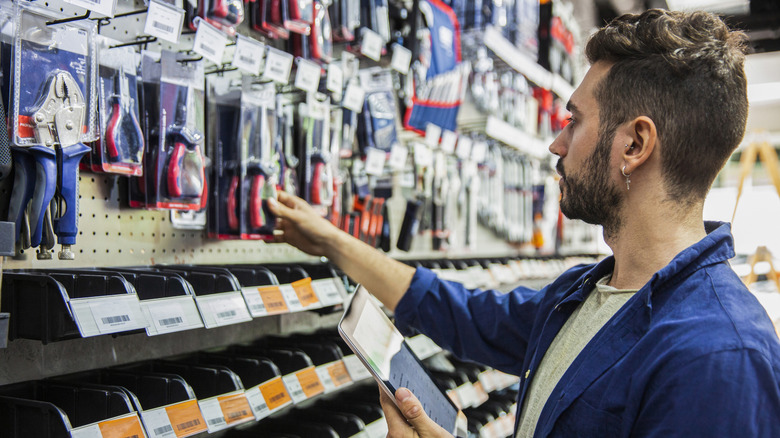Young man in hardware store holding a smartphone with a list open