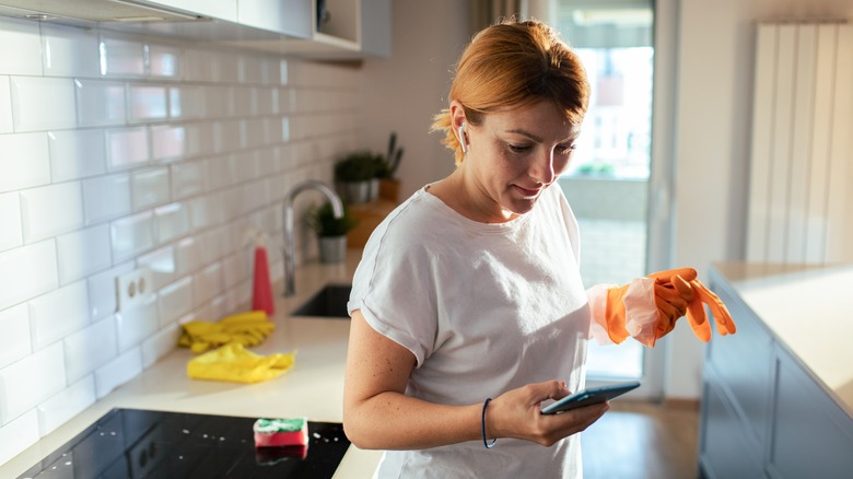 Woman checking smartphone while cleaning the kitchen