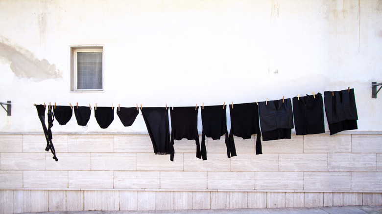 Black clothing hanging on a clothesline in front of a white wall