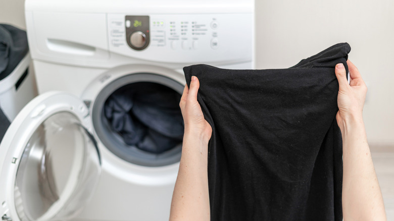 A person holds black clothing in front of the washing machine