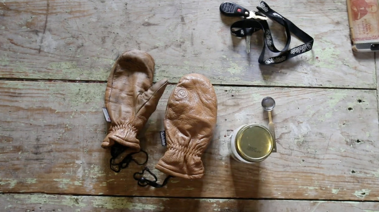 Brown leather mittens sit on a wood countertop after being cleaned and conditioned.