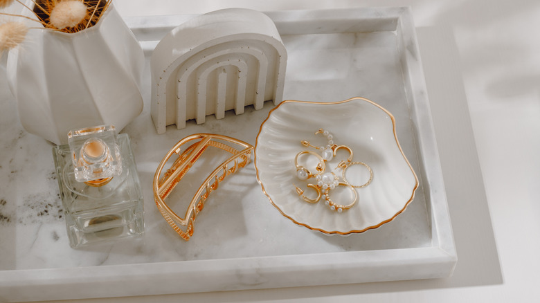 White display tray with trinkets, jewelry, perfume, and hair clip on it