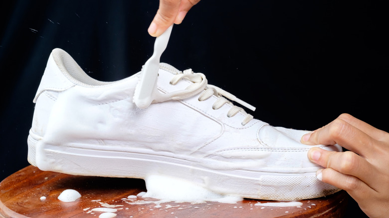 Person washing white sneakers with toothbrush