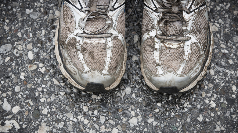 Dirty white running shoes covered in mud on concrete