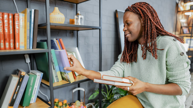 A woman removes excess books from a bookshelf.