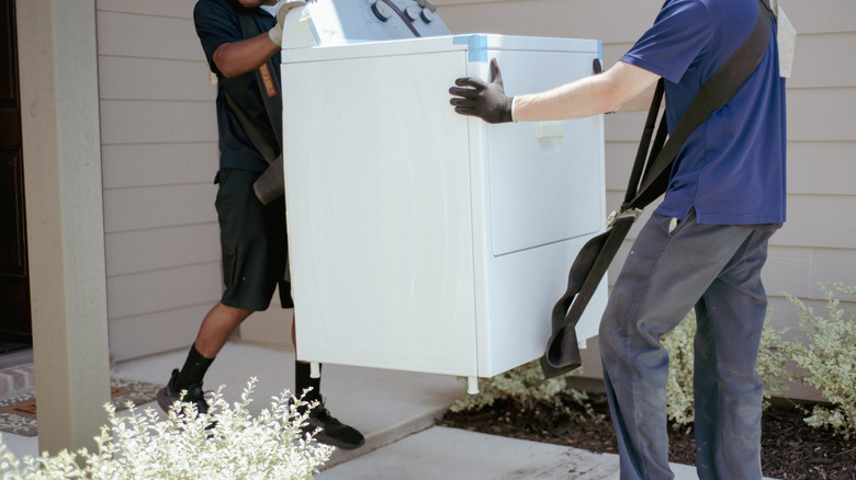 Two people moving a white washing machine.