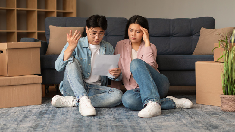 A couple sits by a sofa while looking at their moving checklist