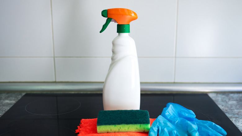 Cleaning spray on a stove next to a sponge, cloth, and gloves