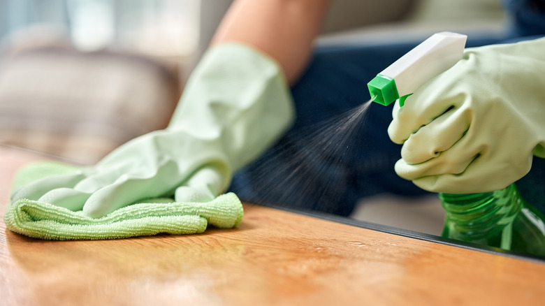A person spraying a cleaner on a wood table and holding a cloth