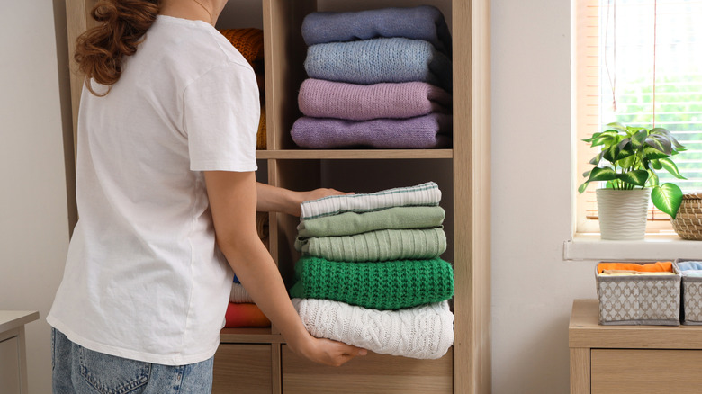 Person putting folded sweaters in a cupboard