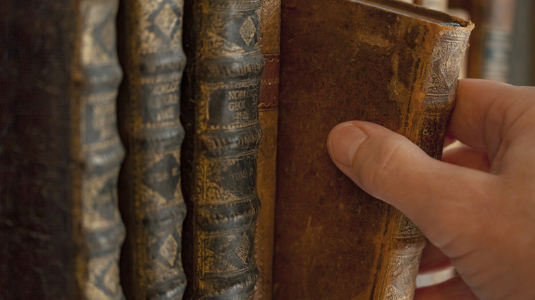 Man's hand pulling an old book from a shelf