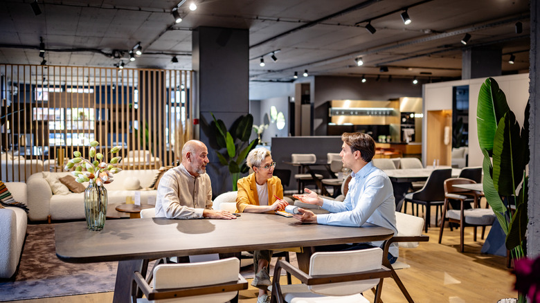 An older couple sitting at a new dining table talking with a salesperson in a furniture store.