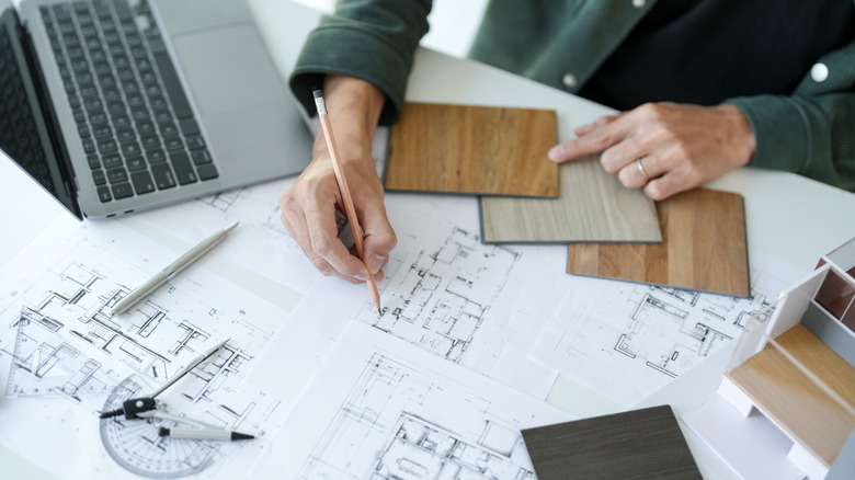 A hand draws floor plan layouts on a table filled with papers