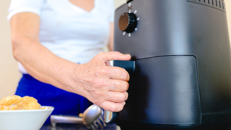 A woman's hand gripping the handle of a black large capacity air fryer to open it