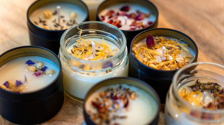 A series of small candles with white wax and dried flowers on top in glass and black containers