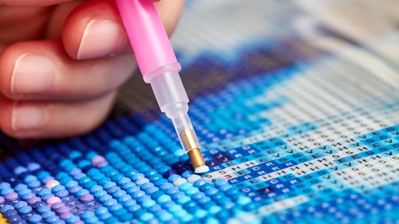 A person adding diamonds onto a labeled canvas with a little pink pen