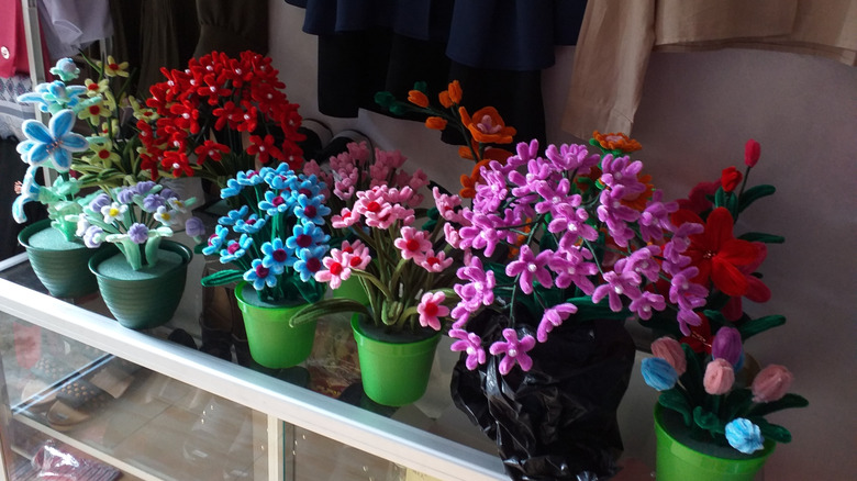 A series of flowers made from pipe cleaners in green pots and foam on a glass shelf