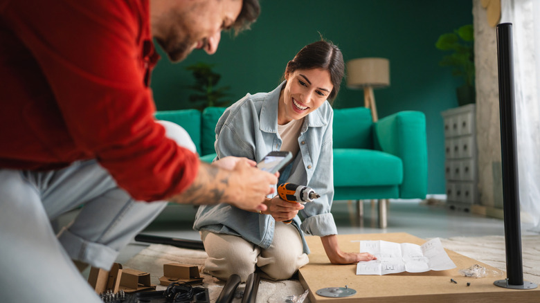 Two people kneeling on the living room floor, using tools to build furniture