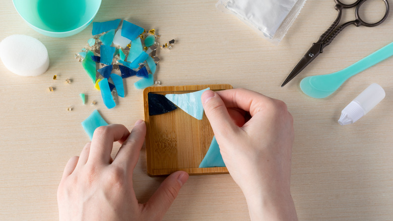 A person creating a mosaic out of broken glass pieces with scraps and tools surrounding them on the table