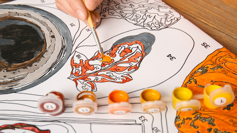 A person painting on a paint by numbers kit showing bright oranges and yellows
