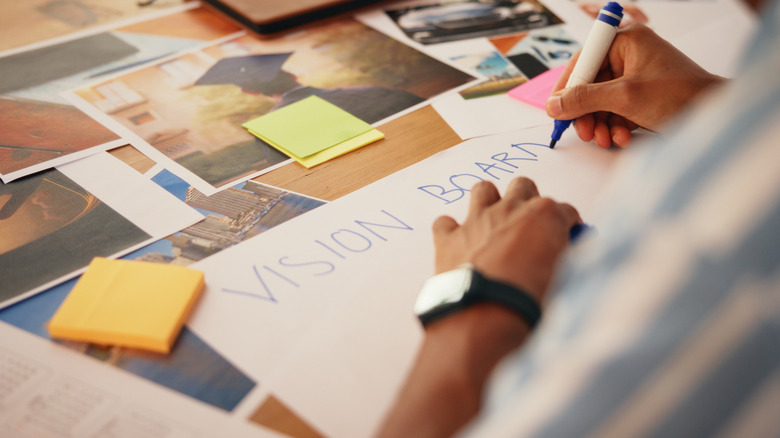 A person creating a vision board with markers, sticky notes, and printed pictures on a wooden table