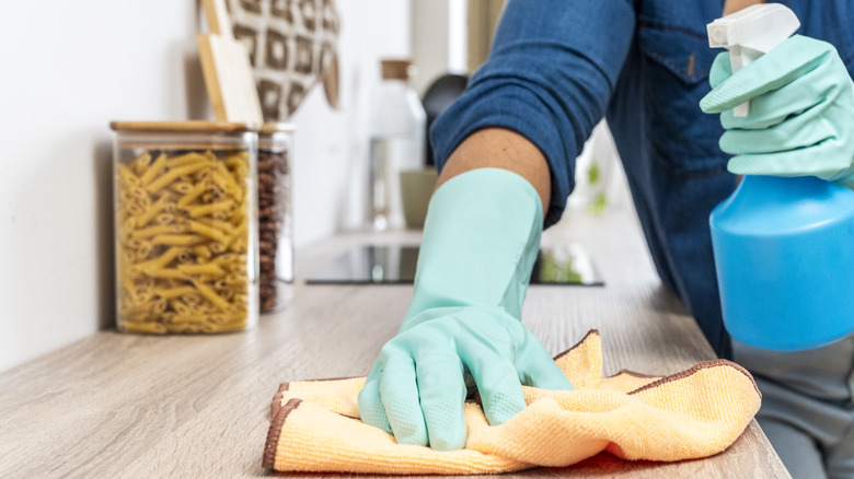 Person uses a disinfectant to wipe down a kitchen countertop with an orange towel.