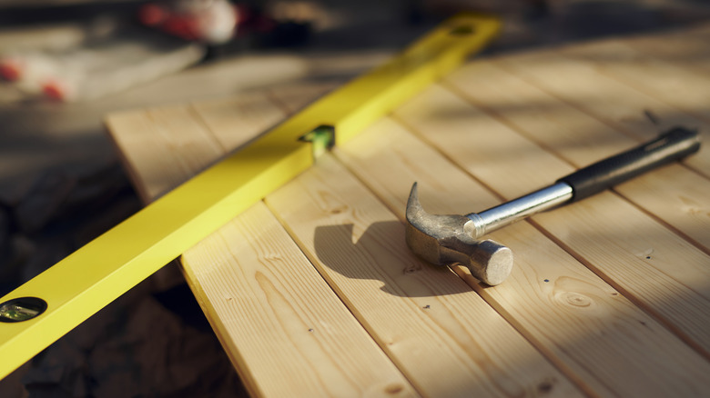A hammer and level laying flat on wood planks