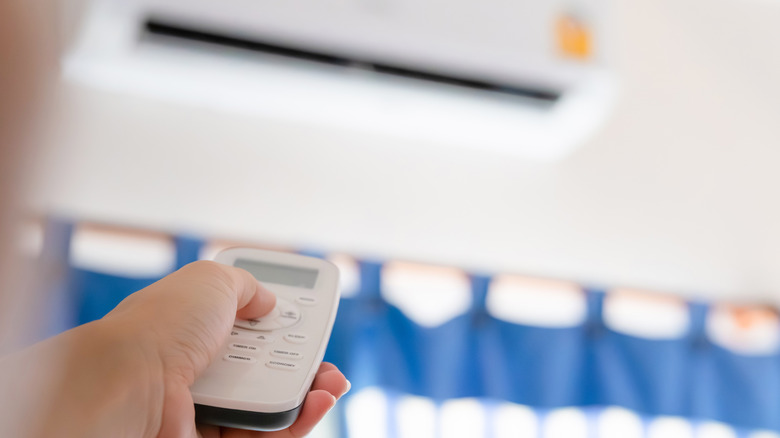 Woman holding remote air conditioner turning on cooler system