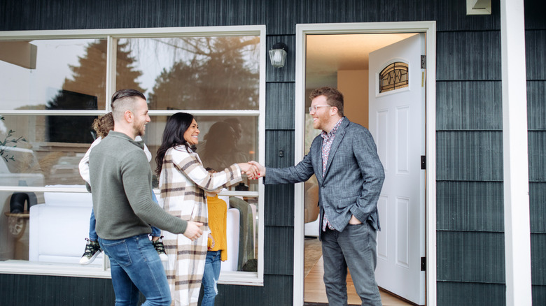 A realtor shades hands with potential homebuyers in front of a black house