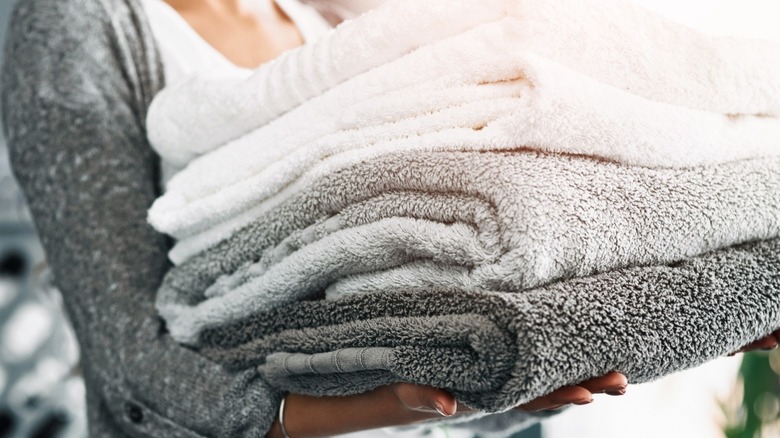 Person holding neatly folded stack of clean white and gray towels.