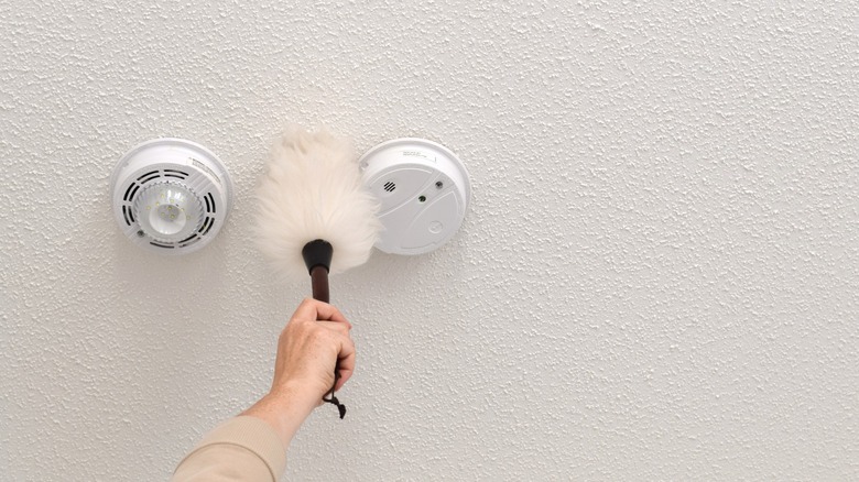 Close-up of woman reaching to feather dust fire alarms and popcorn ceiling