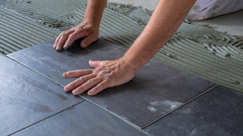A person manually lays tiles down for installation on the floor