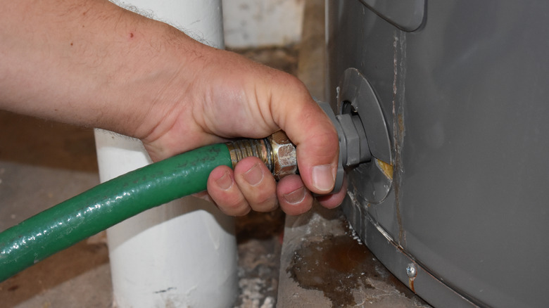 Hand connecting garden hose to water heater