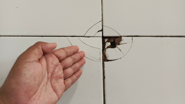A series of cracked tile with a hand pointing at the corner that broke