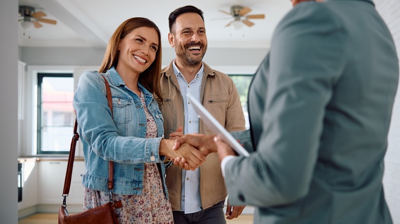 Couple buying new house shaking hands with realtor