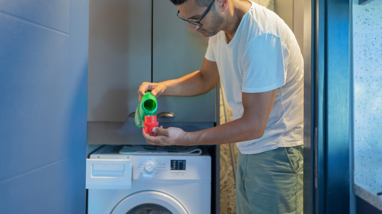 Man in a laundry room measuring liquid detergent in a cup