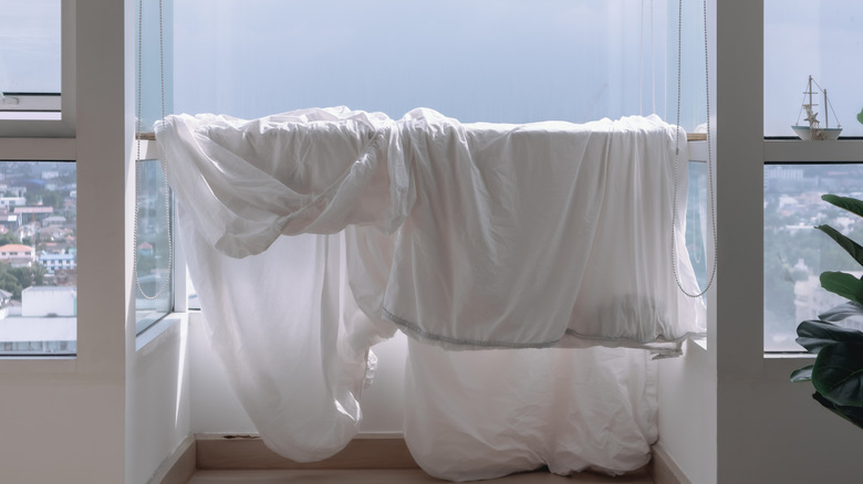 Wet white bed sheets hung over balcony rail to dry