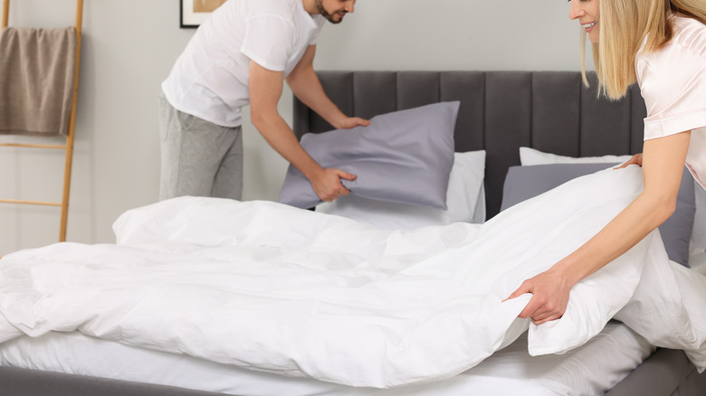 Couple fluffing pillows and arranging duvet in bedroom