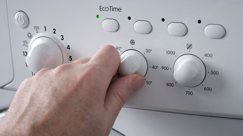Hand turning the temperature knob on a washing machine