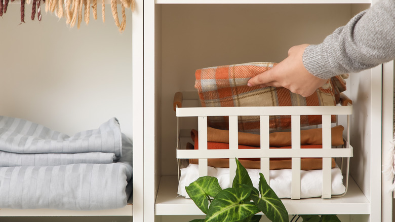 Hand placing washed bed sheets in an open basket in a cupboard