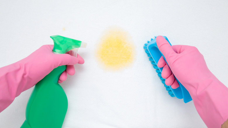 Hands holding cleaning supplies to remove yellow stain from a white sheet