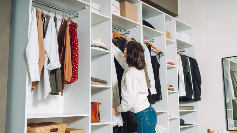A woman reaches up into a well-organized open closet