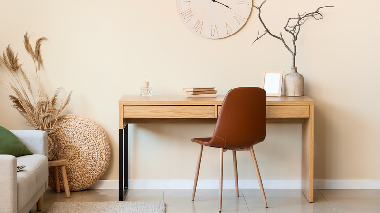 Minimalist living room with clock, natural wood desk, and gray chair.
