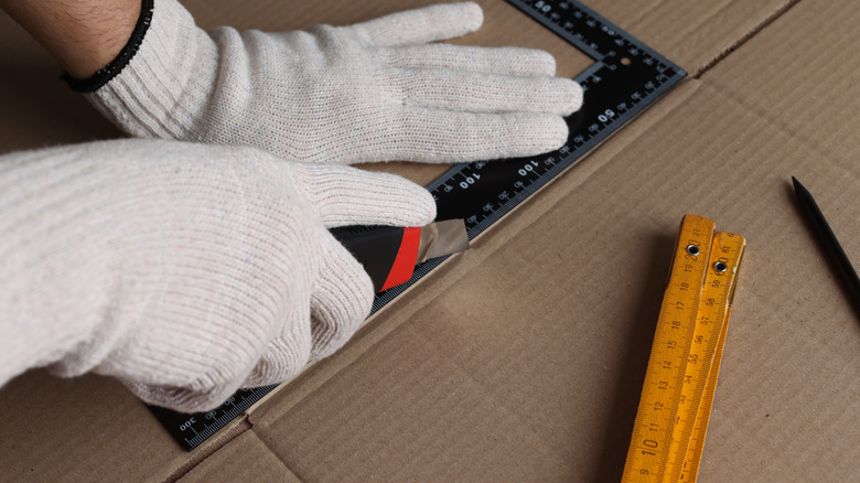 A person scores cardboard using a utility knife and ruler