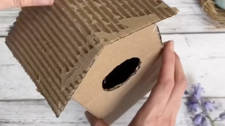 A person glues a roof to a cardboard bird house