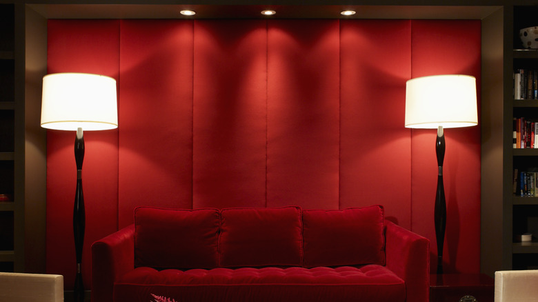 A red couch against a red wall surrounded by two white lamps