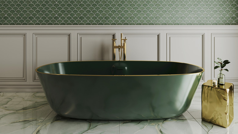 Green stand-alone tub with a gold rim in a modern bathroom with green fishscale walls and a gold side table